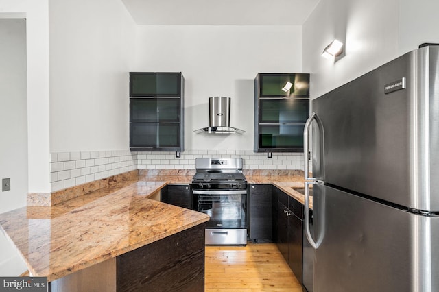 kitchen with backsplash, wall chimney range hood, kitchen peninsula, light stone countertops, and appliances with stainless steel finishes