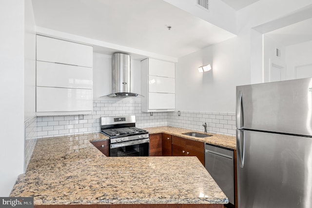 kitchen with appliances with stainless steel finishes, wall chimney range hood, light stone counters, and white cabinetry