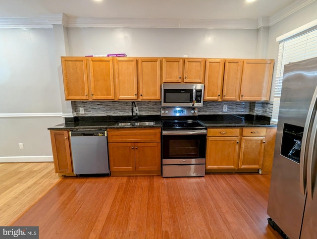 kitchen featuring sink, light wood-type flooring, dark stone countertops, ornamental molding, and stainless steel appliances