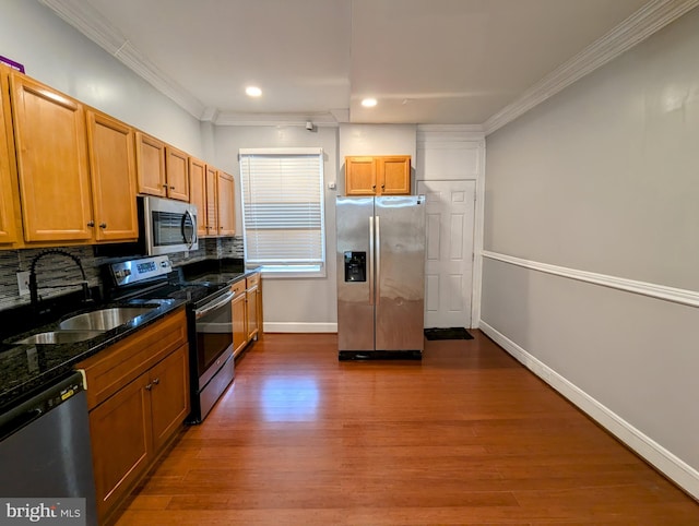 kitchen with crown molding, appliances with stainless steel finishes, dark hardwood / wood-style floors, dark stone counters, and backsplash