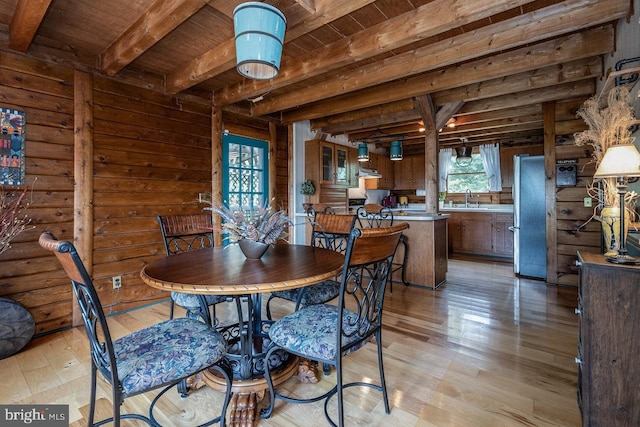 dining area with sink, beamed ceiling, rustic walls, light hardwood / wood-style flooring, and wooden ceiling