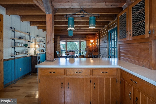 kitchen featuring wood walls, beam ceiling, kitchen peninsula, light hardwood / wood-style flooring, and hanging light fixtures