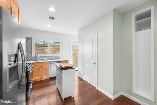 kitchen featuring tasteful backsplash, stainless steel appliances, light brown cabinets, dark hardwood / wood-style floors, and a center island