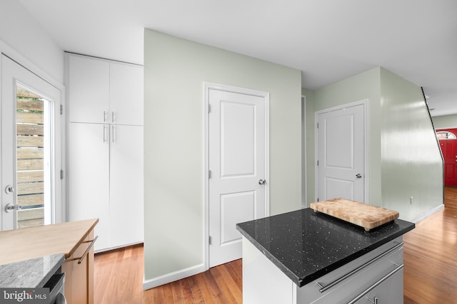 kitchen featuring dark stone countertops, a kitchen island, white cabinetry, and light wood-type flooring