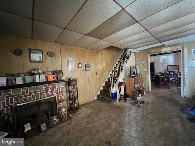 carpeted living room with a paneled ceiling, wood walls, and a fireplace