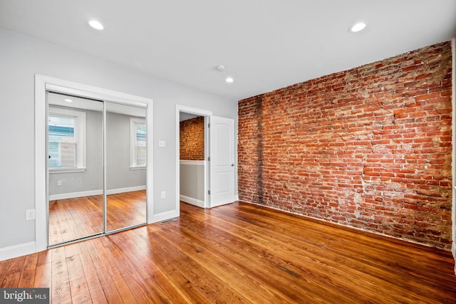 unfurnished bedroom with hardwood / wood-style flooring, brick wall, and a closet