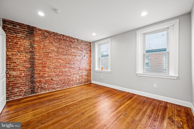 empty room featuring wood-type flooring and brick wall