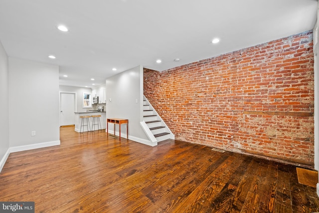 unfurnished living room featuring brick wall and wood-type flooring