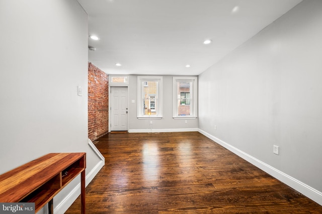 unfurnished living room featuring brick wall and dark hardwood / wood-style floors