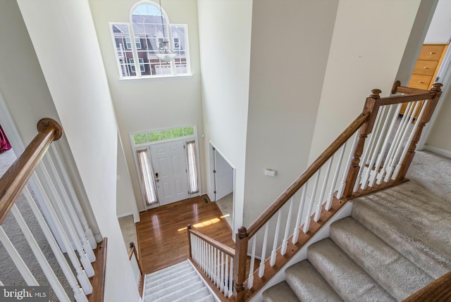 stairway featuring baseboards, a high ceiling, and wood finished floors