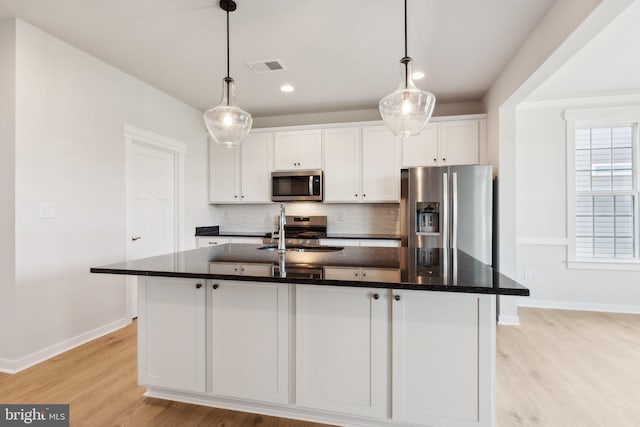 kitchen with appliances with stainless steel finishes, decorative light fixtures, a kitchen island with sink, white cabinets, and sink