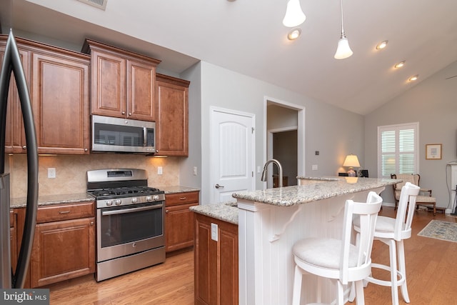 kitchen featuring decorative backsplash, appliances with stainless steel finishes, vaulted ceiling, light hardwood / wood-style floors, and a kitchen island