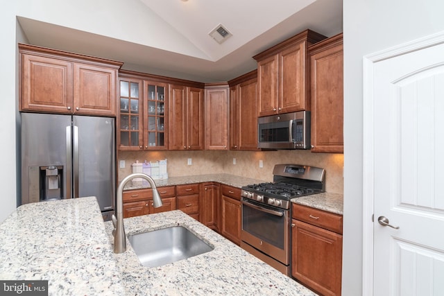 kitchen featuring lofted ceiling, stainless steel appliances, decorative backsplash, sink, and light stone counters