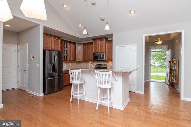 kitchen featuring light hardwood / wood-style flooring, stainless steel appliances, a kitchen breakfast bar, an island with sink, and tasteful backsplash