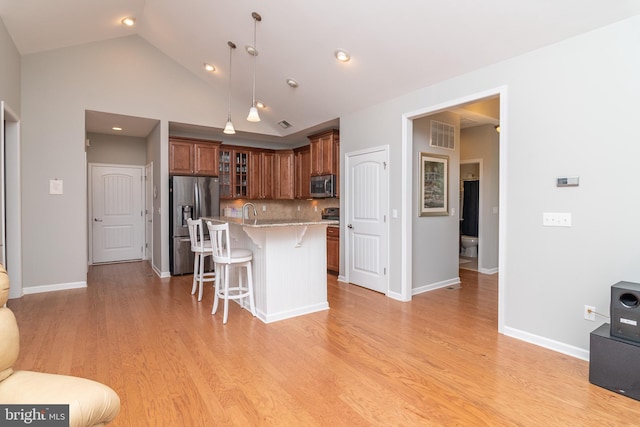 kitchen with appliances with stainless steel finishes, pendant lighting, backsplash, light wood-type flooring, and a breakfast bar area