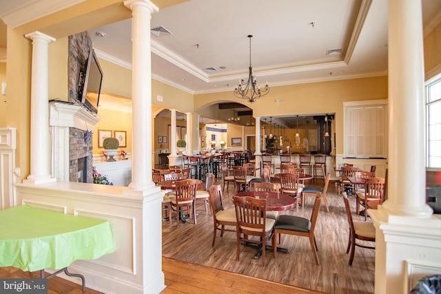 dining room with a raised ceiling, crown molding, a notable chandelier, ornate columns, and wood-type flooring