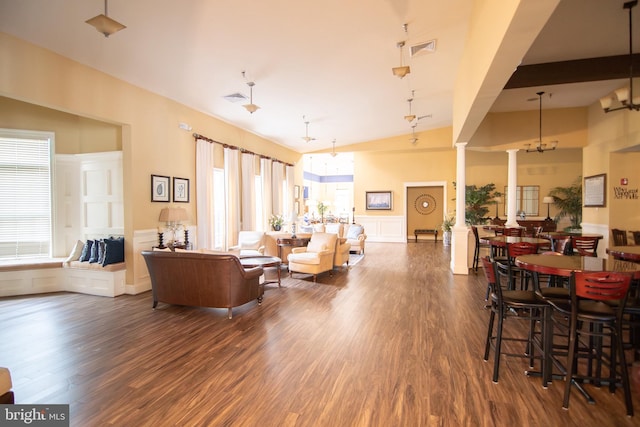 living room with decorative columns, high vaulted ceiling, dark hardwood / wood-style floors, and an inviting chandelier