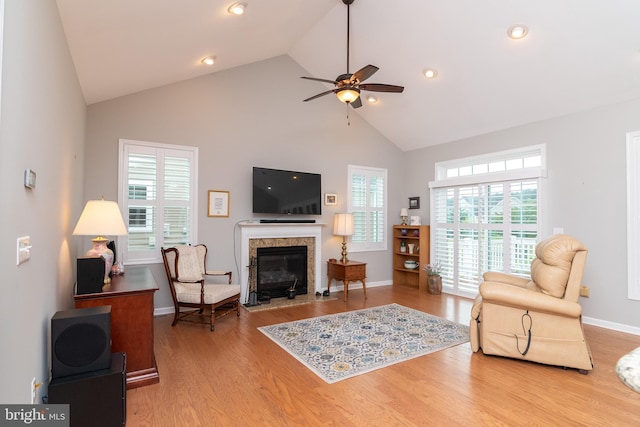 living room with ceiling fan, a high end fireplace, high vaulted ceiling, and light hardwood / wood-style flooring