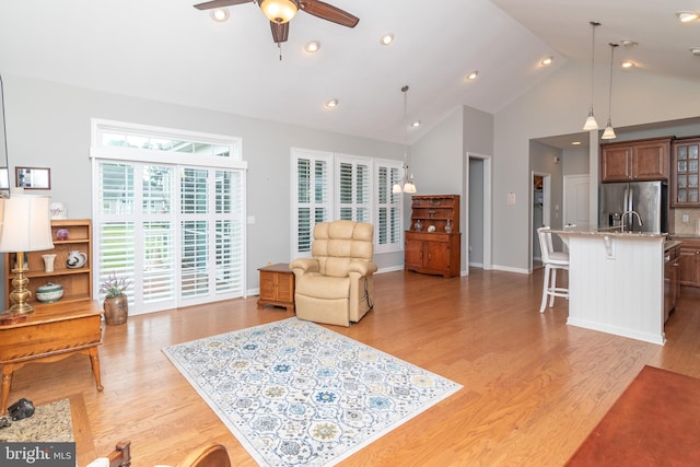 living room with ceiling fan, high vaulted ceiling, and light hardwood / wood-style flooring