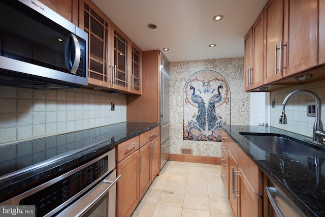 kitchen with light tile patterned flooring, sink, dark stone countertops, stainless steel appliances, and decorative backsplash