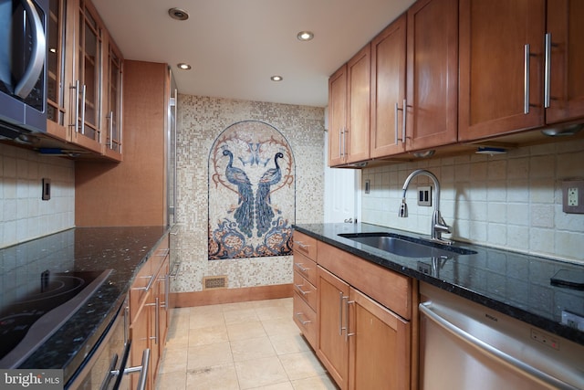 kitchen with appliances with stainless steel finishes, sink, dark stone countertops, backsplash, and light tile patterned floors