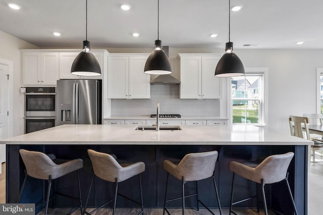 kitchen with appliances with stainless steel finishes, decorative light fixtures, a large island with sink, and white cabinets