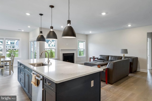 kitchen featuring sink, an island with sink, decorative light fixtures, stainless steel dishwasher, and light wood-type flooring