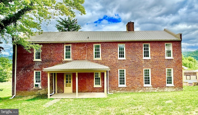 back of house with a patio area, a chimney, brick siding, and a yard