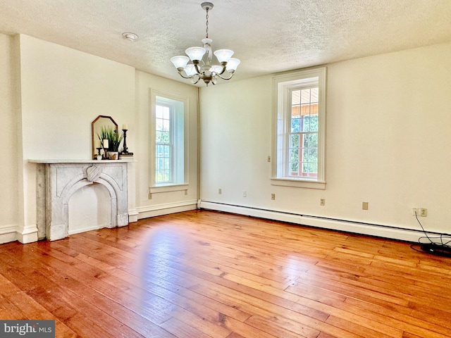 unfurnished living room featuring light wood-type flooring, a textured ceiling, baseboard heating, and a chandelier