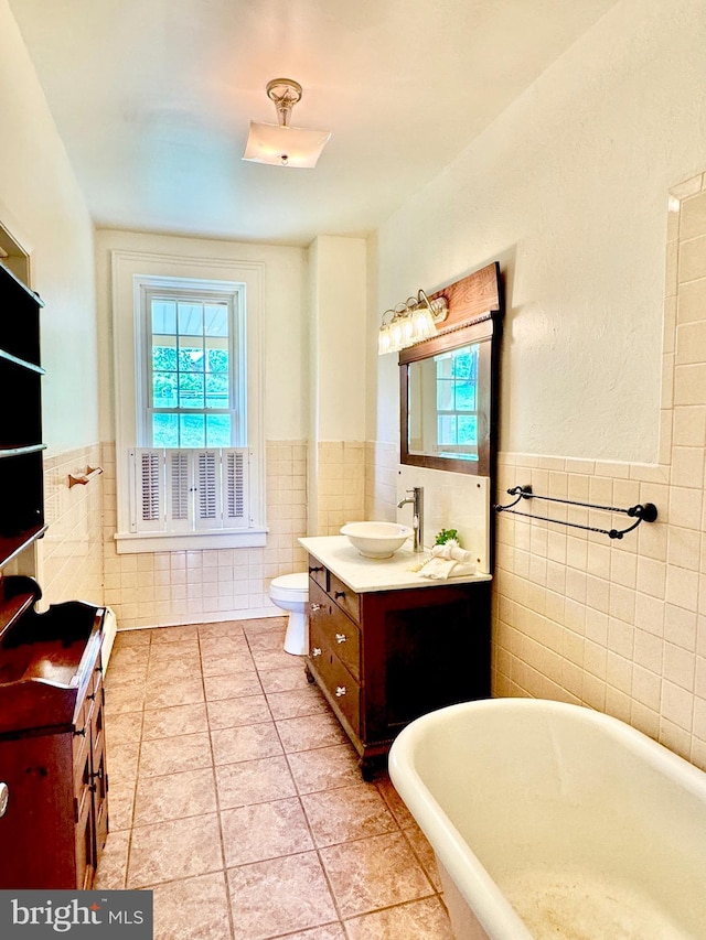 bathroom with tile walls, wainscoting, vanity, tile patterned flooring, and a freestanding tub