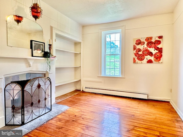 living room featuring a tile fireplace, hardwood / wood-style floors, built in shelves, baseboard heating, and a textured ceiling