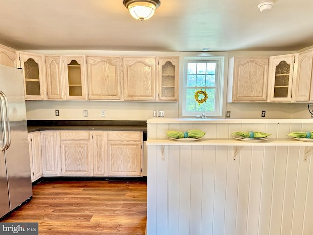 kitchen with glass insert cabinets, dark countertops, wood finished floors, and stainless steel refrigerator