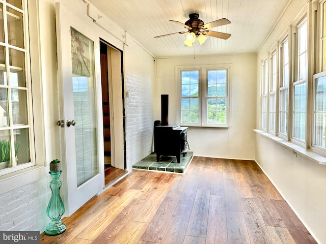 unfurnished sunroom with a wood stove and ceiling fan