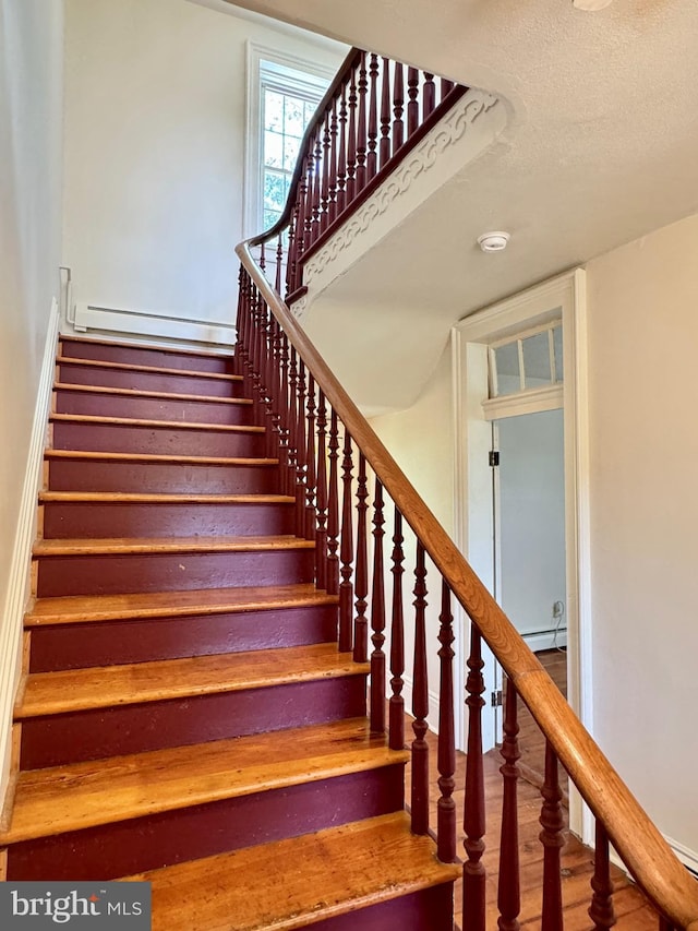 stairs with a baseboard heating unit, a textured ceiling, and hardwood / wood-style flooring