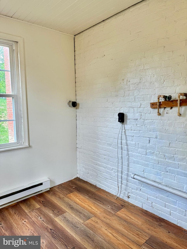 unfurnished room featuring a healthy amount of sunlight, a baseboard radiator, brick wall, and hardwood / wood-style floors