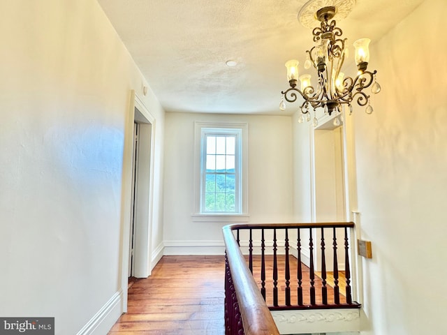 hallway with a textured ceiling, hardwood / wood-style floors, an inviting chandelier, and baseboards