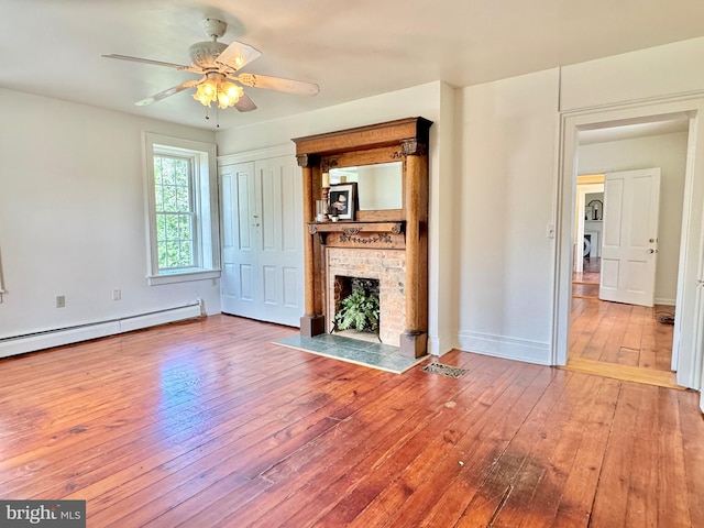 unfurnished living room with baseboard heating, ceiling fan, hardwood / wood-style flooring, and a fireplace