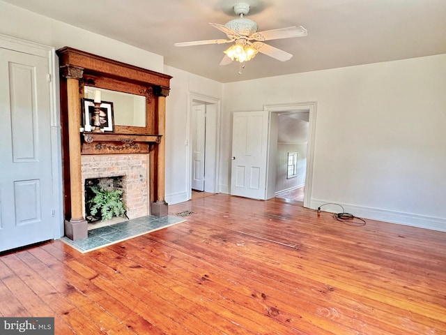 unfurnished living room with wood-type flooring, a brick fireplace, and ceiling fan