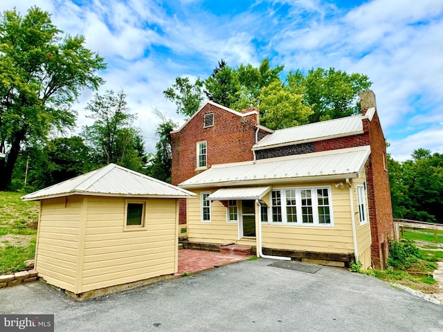 back of house with entry steps, a chimney, metal roof, an outbuilding, and a patio area