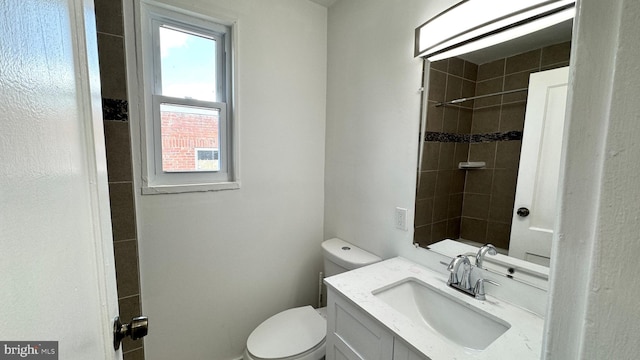 bathroom featuring toilet, a healthy amount of sunlight, tiled shower, and vanity