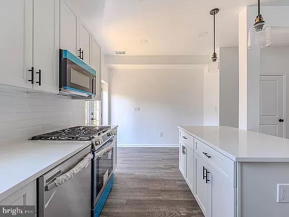 kitchen featuring white cabinets, decorative light fixtures, dark hardwood / wood-style flooring, stainless steel appliances, and decorative backsplash