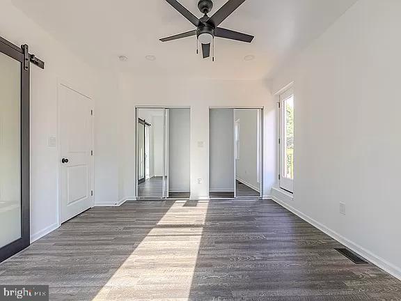 unfurnished bedroom featuring ceiling fan, dark hardwood / wood-style flooring, two closets, and a barn door