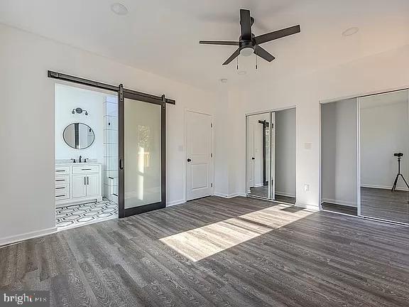 interior space featuring ceiling fan, ensuite bath, dark hardwood / wood-style floors, and two closets