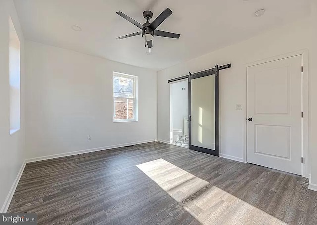 unfurnished bedroom with ceiling fan, a barn door, and dark hardwood / wood-style floors