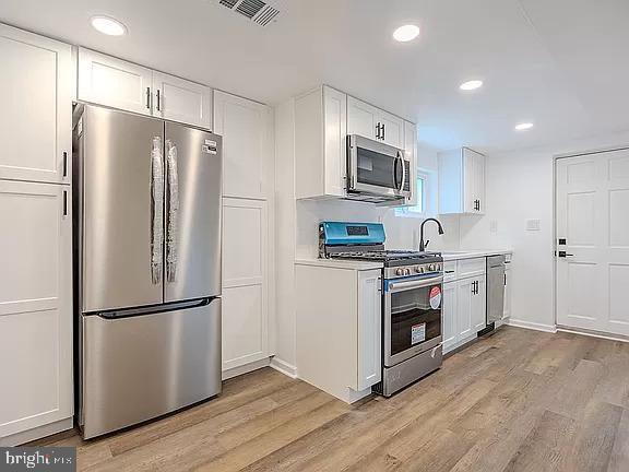 kitchen with white cabinets, light wood-type flooring, appliances with stainless steel finishes, and sink