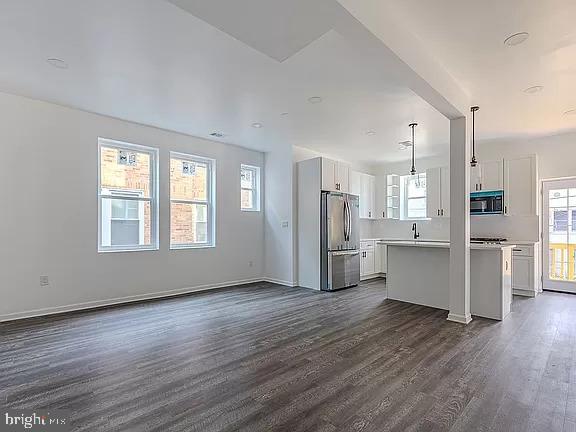 kitchen featuring white cabinets, a kitchen island, dark wood-type flooring, hanging light fixtures, and stainless steel refrigerator