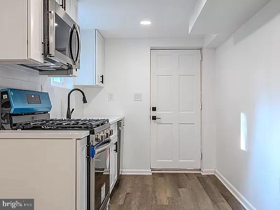 kitchen with dark wood-type flooring, backsplash, white cabinets, and stainless steel appliances