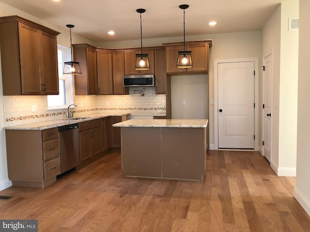 kitchen with sink, a center island, hanging light fixtures, stainless steel appliances, and light stone countertops