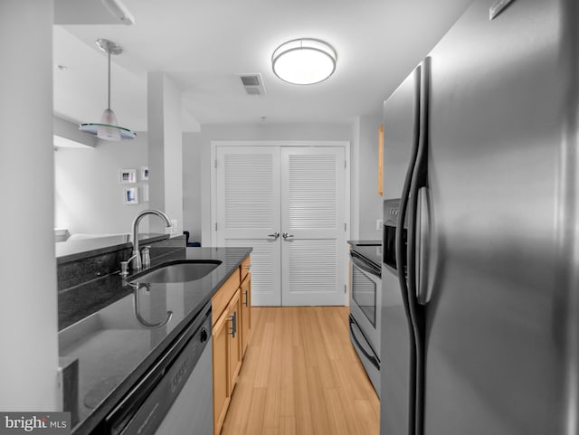 kitchen with pendant lighting, sink, dark stone countertops, light hardwood / wood-style floors, and appliances with stainless steel finishes