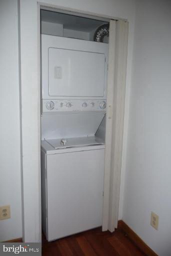 laundry room with stacked washer and clothes dryer and wood-type flooring